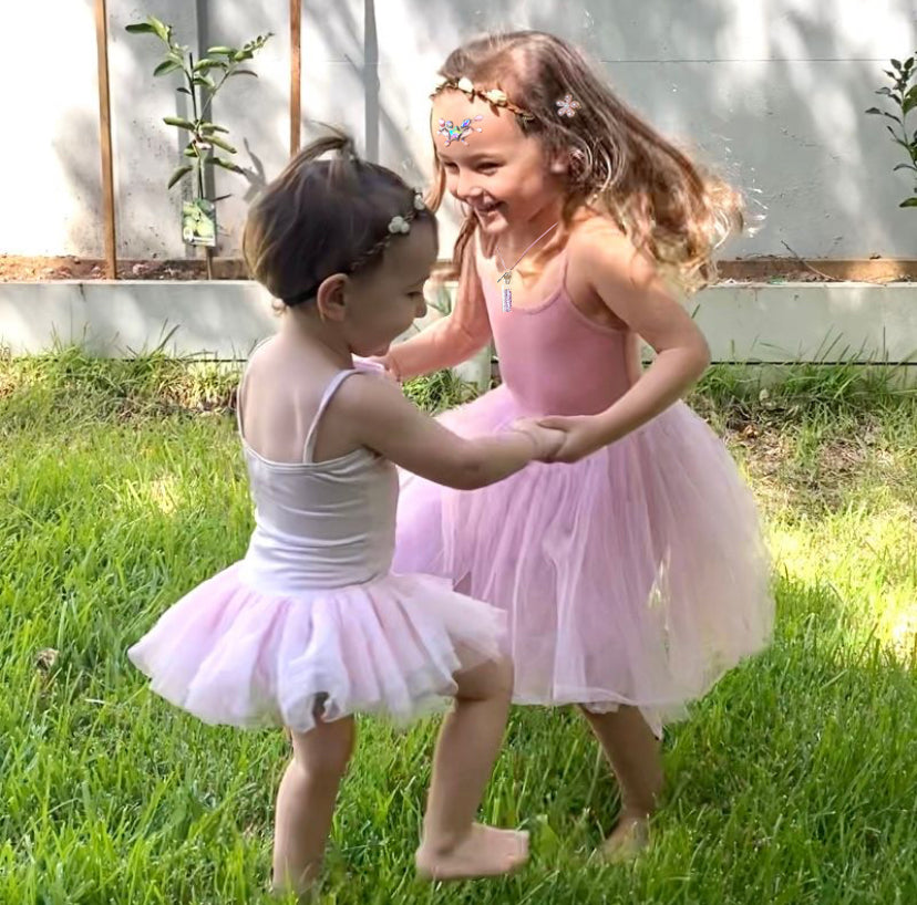 Two young girls in ballet outfits dancing outdoors on grass.